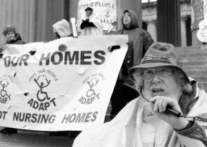 Bob Kafka, an older white man with curly white hair and a long white beard, speaks at an ADAPT protest 