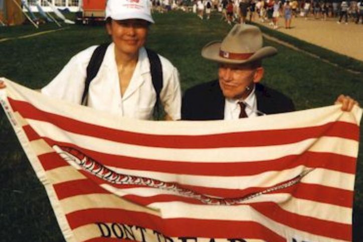 person in white shirt and white hat standing with person wearing suite and cowboy hat holding a flag